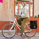 Eine Frau fährt mit dem Fahrrad durch die Stadt, während das schwarze WEATHERGOODS SWEDEN Bikepack sicher als Seitentasche am Gepäckträger montiert ist.